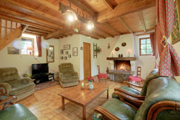 Salon rustique et confortable avec une chemin&eacute;e chaleureuse, des poutres en bois et des fauteuils verts confortables, cr&eacute;ant une atmosph&egrave;re invitante pour la d&eacute;tente et la planification d'un week-end de chasse.
