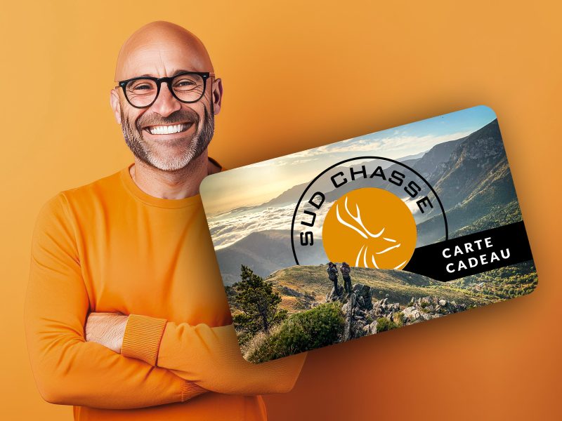 Smiling bald man in an orange jumper presenting a gift card with a mountainous outdoor landscape and a hunting logo.