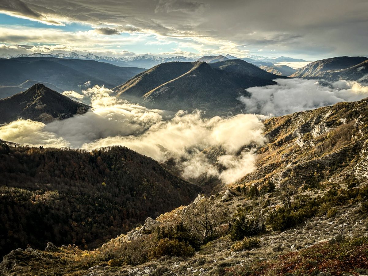 Breathtaking views from the top of a mountain, as clouds roll across the valleys like a river flowing under a dramatic sky, with distant peaks witnessing the spectacle on a hunting weekend in the Pyrenees.