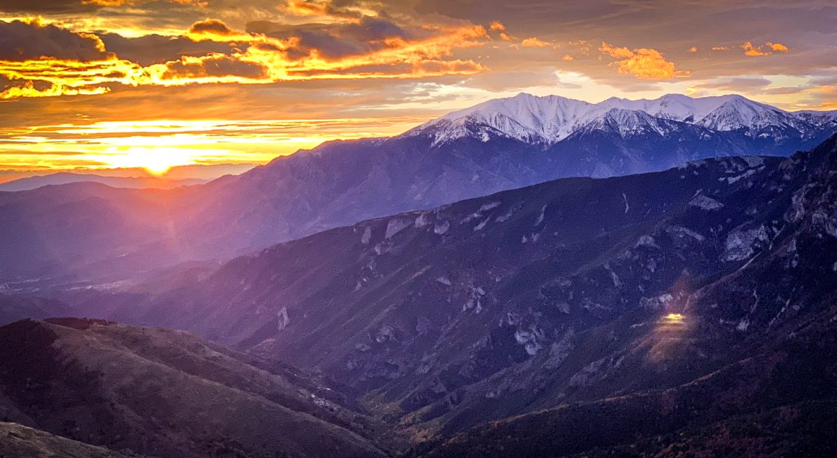 A breathtaking sunset paints the sky in warm hues over a craggy mountain range, the last rays of the sun casting a golden glow over the snow-capped peaks.