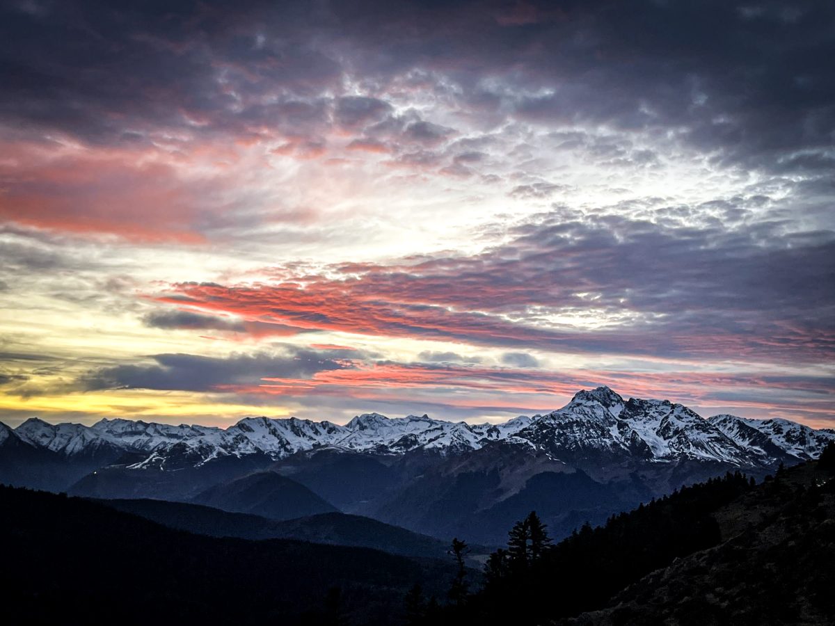 A spectacular sunset painting the sky in shades of orange and pink over a majestic mountain range, with jagged peaks against a vibrant backdrop, evoking the charm of hunting in the Pyrenees.
