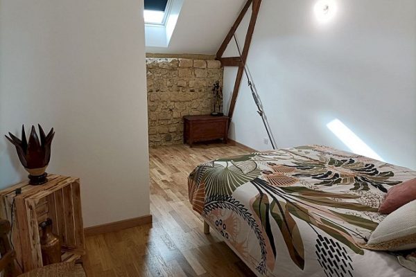 Cosy attic room with tropical-themed bedspread, exposed beams and period stone wall, creating a blend of rustic charm and modern comforts for an idyllic hunting break