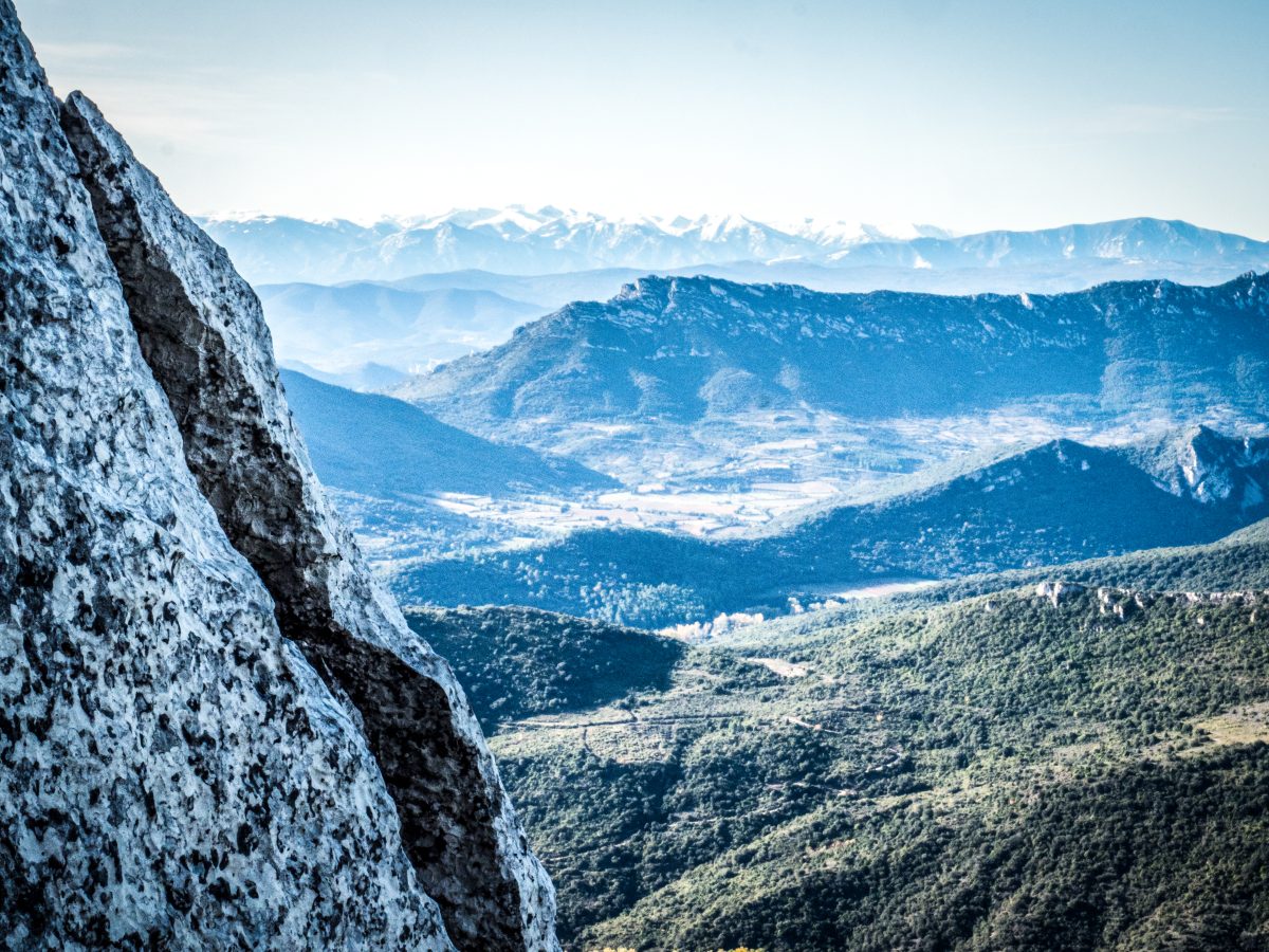 Montañas nevadas a lo lejos vistas desde un mirador rocoso, con vistas a un vasto valle con una atmósfera brumosa.