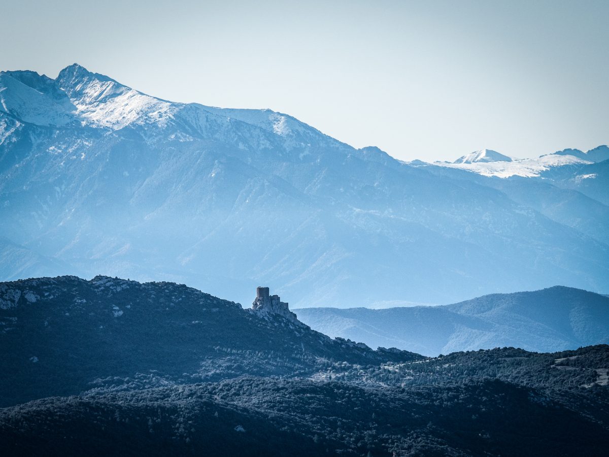 Una estructura solitaria se destaca sobre un fondo de crestas montañosas superpuestas, con picos cubiertos de nieve bajo un cielo azul claro.