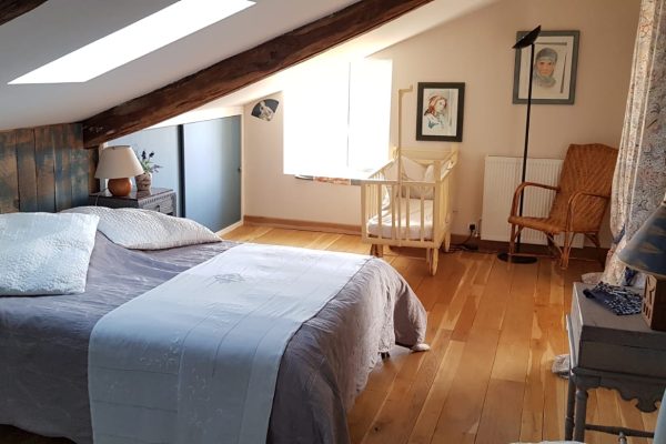 Cosy attic room with sloping ceiling, featuring a comfortable bed, wooden furniture and a warmly lit reading area by the window, perfect for planning hunting trips.