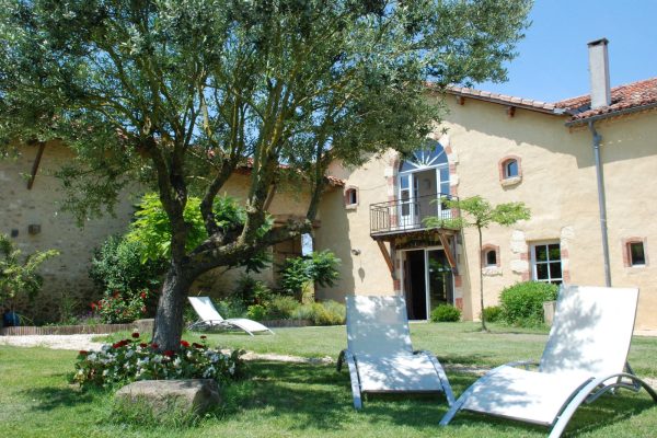 Après-midi ensoleillé et tranquille dans une charmante maison de campagne avec chaises longues prête pour une journée de détente au milieu d'une verdure luxuriante, parfaite pour un séjour de chasse en France.